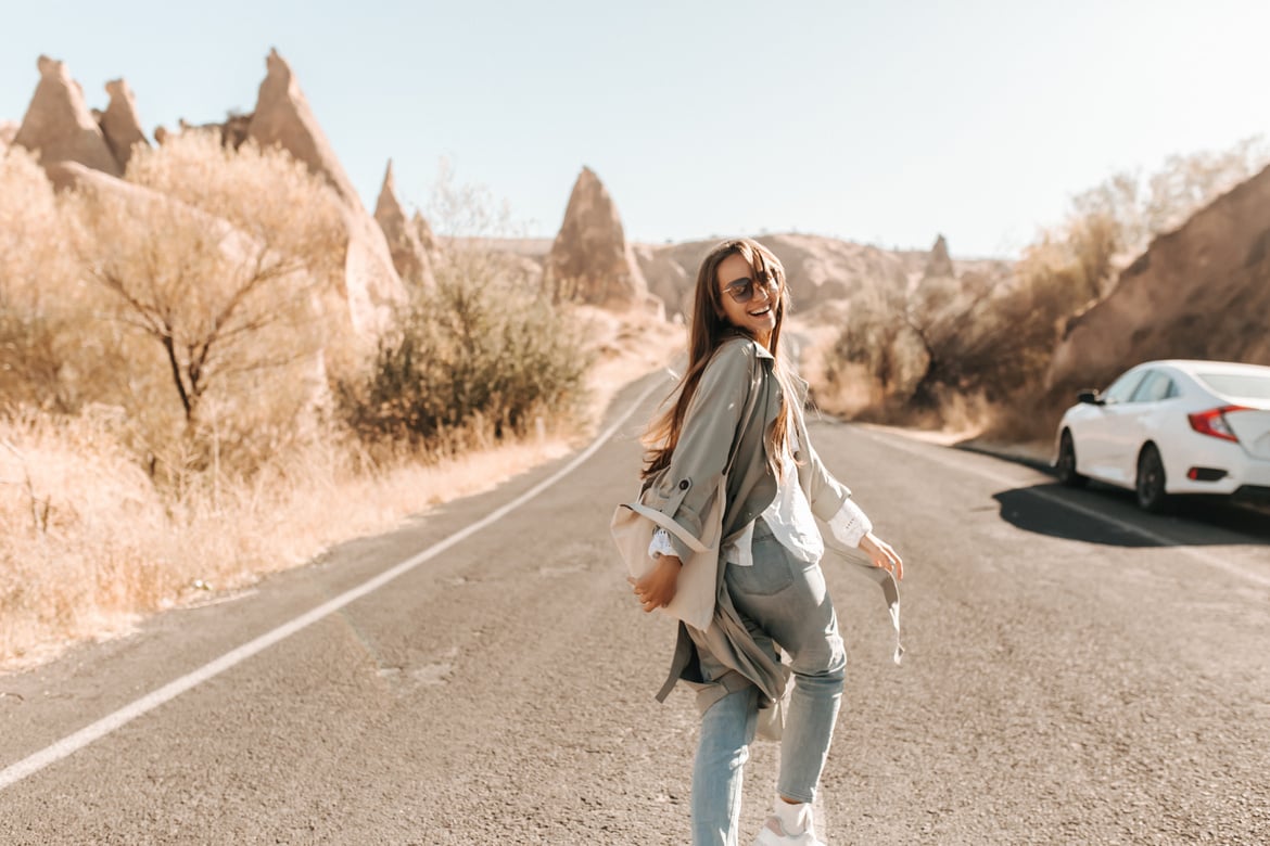 Woman in Beige Trench Coat Walking on Asphalt Road